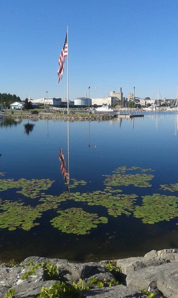 Flag in Alpena harbor reflected in the still water on August 1, 2016