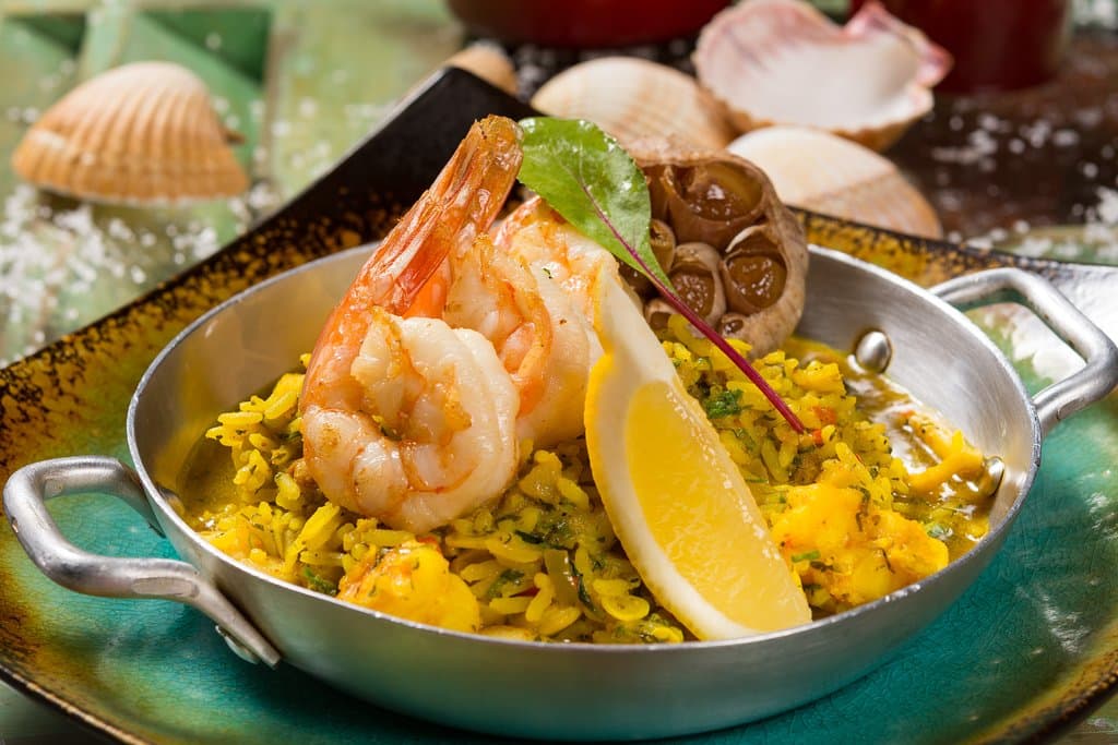 Arroz caldoso de camarão, peixe branco e lulas cozidas no açafrão goiano com linguiça suína caseira Universal e alho argentino assado por horas no azeite extravirgem.