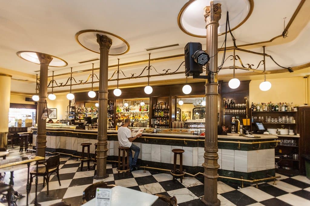 Una barra luminosa y clara, definida por su frontal de espejos y botilleros de madera y cristal como corresponde a un establecimiento consolidado por la Historia.