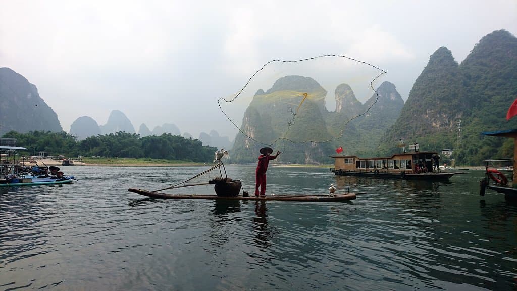 黃布灘漁翁泛舟江上，熟練地在桂林山水美景下撒網捕魚景觀