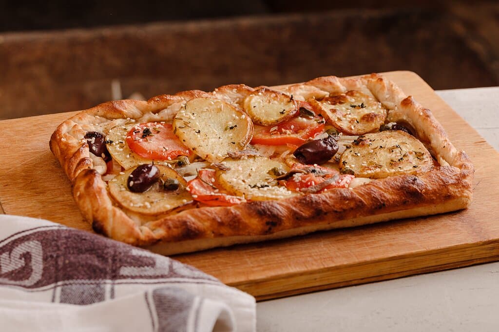 Karmni s-Sultana

Maltese bread dough topped with thin sliced potatoes, tomatoes, anchovies, onions, capers, olives, fresh mint, fennel seeds and sesame seeds.