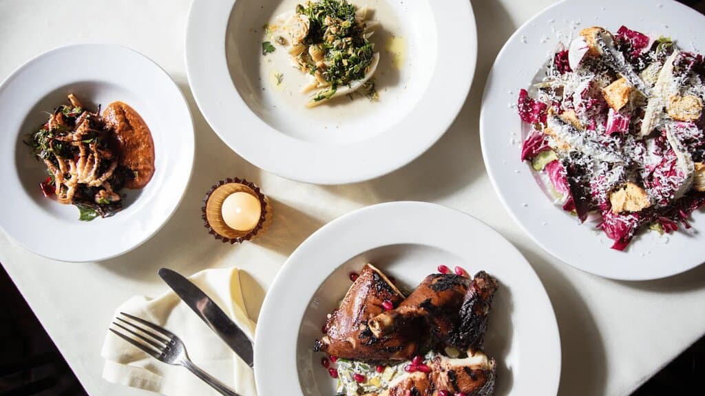 An overhead shot of four meals on white plates: chicken, fennel, radicchio, and octopus, with pomegranates, parmesan, and romesco.

Photo Credit: https://www.gabonghi.com/ & https://philly.eater.com/22934864/mish-mish-philly-alex-tewfik-philly-mag-reservations