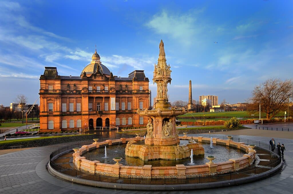 An exterior view of the People's Palace museum on Glasgow Green, with the Doulton Fountain in the foreground. The People's Palace is a red sandstone Victorian building dating and the fountain is terracotta. 