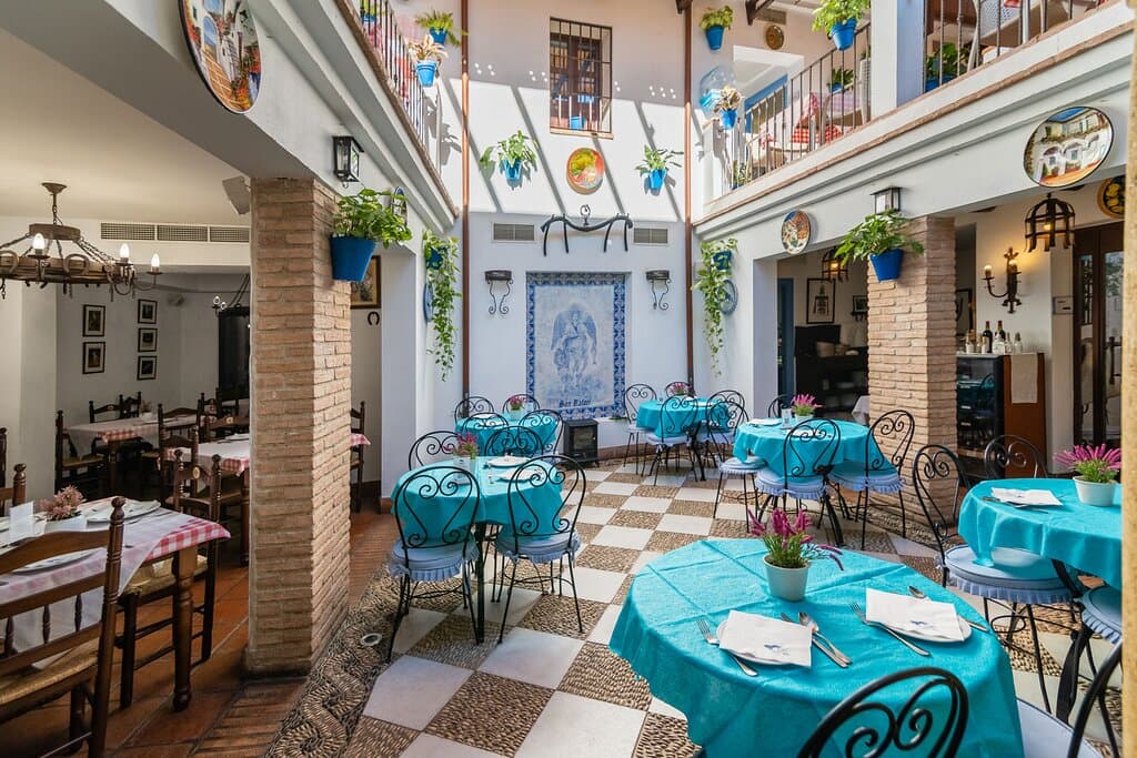 Esta encantadora posada encuentra su hogar en una antigua casa del siglo XV, lo que le confiere un ambiente histórico y auténtico. Justo al lado de las Caballerizas Reales, el restaurante se sumerge en la rica historia de la ciudad, ofreciendo a sus comensales una experiencia única que va más allá de simplemente disfrutar de una comida.