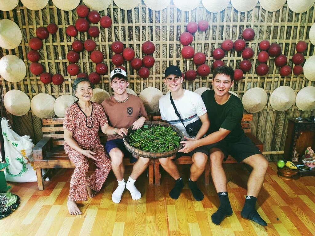 Du khách nước ngoài đang vui vẻ tham gia vào hoạt động truyền thống cùng với người địa phương. Tại Cồn Sơn du khách có thể trải nghiệm làm bánh dân gian giữa khung cảnh làng quê mộc mạc.