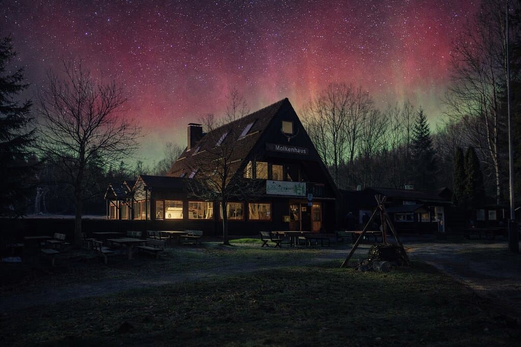 Das Molkenhaus Bad Harzburg bei Nacht, stimmungsvoll beleuchtet und eingebettet in die Natur des Harzes. Über dem Gebäude zeigen sich farbige Polarlichter am Himmel und verleihen der Szene eine besondere, ruhige Atmosphäre mitten im Nationalpark Harz.