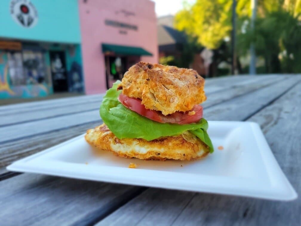 Bacon Cheddar Breakfast Sammie. Bacon cheddar biscuit with fried farm egg*, tomato, lettuce, brown mustard