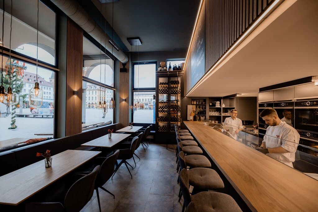 Kulinarischer Treffpunkt auf dem Marktplatz in Würzburg
„Ganz früher war in diesen Räumen die Würzburger Markthalle und dieser Gedanke hat mich inspiriert.“ (Bernhard Reiser)
„Aifach REISERS“ lässt sich mit einem Begriff oder einem einzigen Konzept nicht erfassen. Dieser Ort verändert im Laufe des Tages seine Stimmung, sein Angebot und natürlich auch seine Gäste: Ein genussvolles Fluidum also, eine Wandelbar, ein guter Ort für Würzburg.
Das „Aifach“ folgt einer komplett anderen gastronomischen