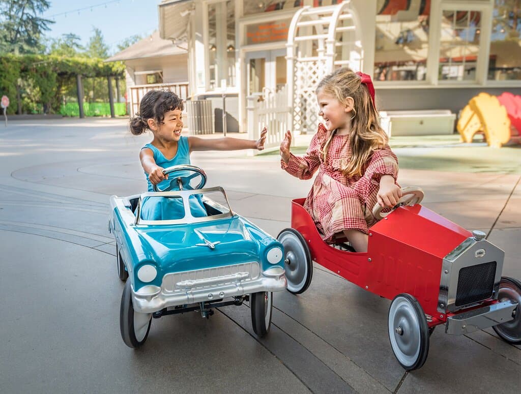 Two children high-fiving in play cars