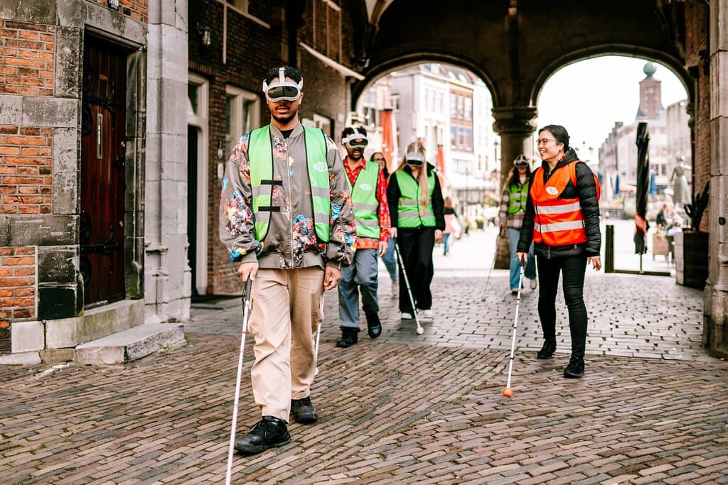 Een groep mensen die een AR bril op hebben waardoor ze ervaren hoe het is om slechtziend te zijn. Ze lopen samen met een slechtziende gids en een taststok door het centrum van Nijmegen.