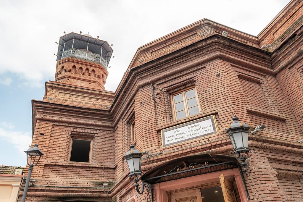Tbilisi Juma Mosque: A Harmonious Blend of Old and New
This captivating image showcases the Tbilisi Juma Mosque, a historic landmark that beautifully blends traditional Islamic architecture with modern elements. The mosque's imposing minaret, a testament to its enduring faith, soars above the city's skyline, while the warm, red-brick exterior and elegant lantern lights create a welcoming ambiance. Discover the rich cultural heritage of Tbilisi & experience the unique charm of this architecture!