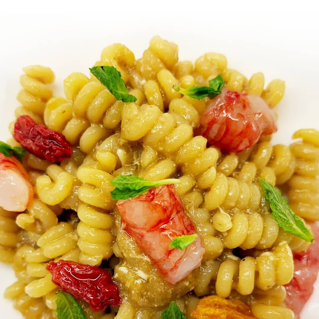 Fusillo Pastificio dei Campi con gambero rosso di Mazara, bisque di gambero e melanzane per un tocco di cremosità. Finiscono il piatto delle freschissime cimette di menta e pomodorini del Piennolo semi-dry.